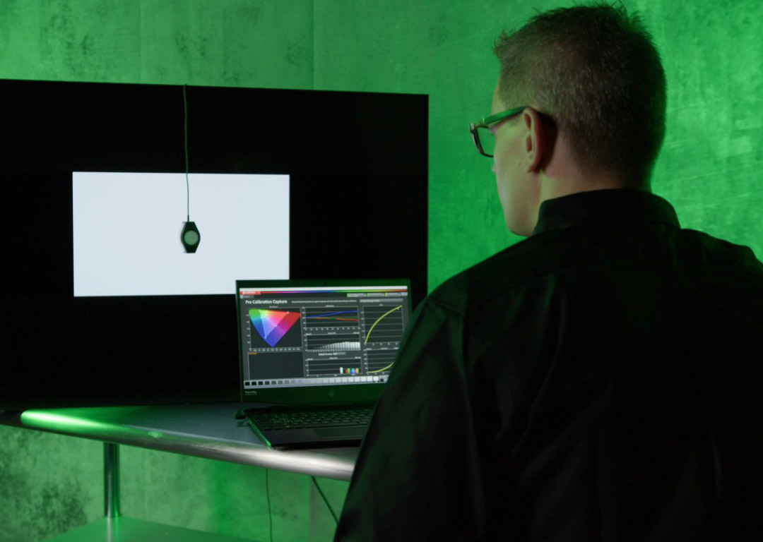person calibrating a tv with laptop and calman in front of green backdrop